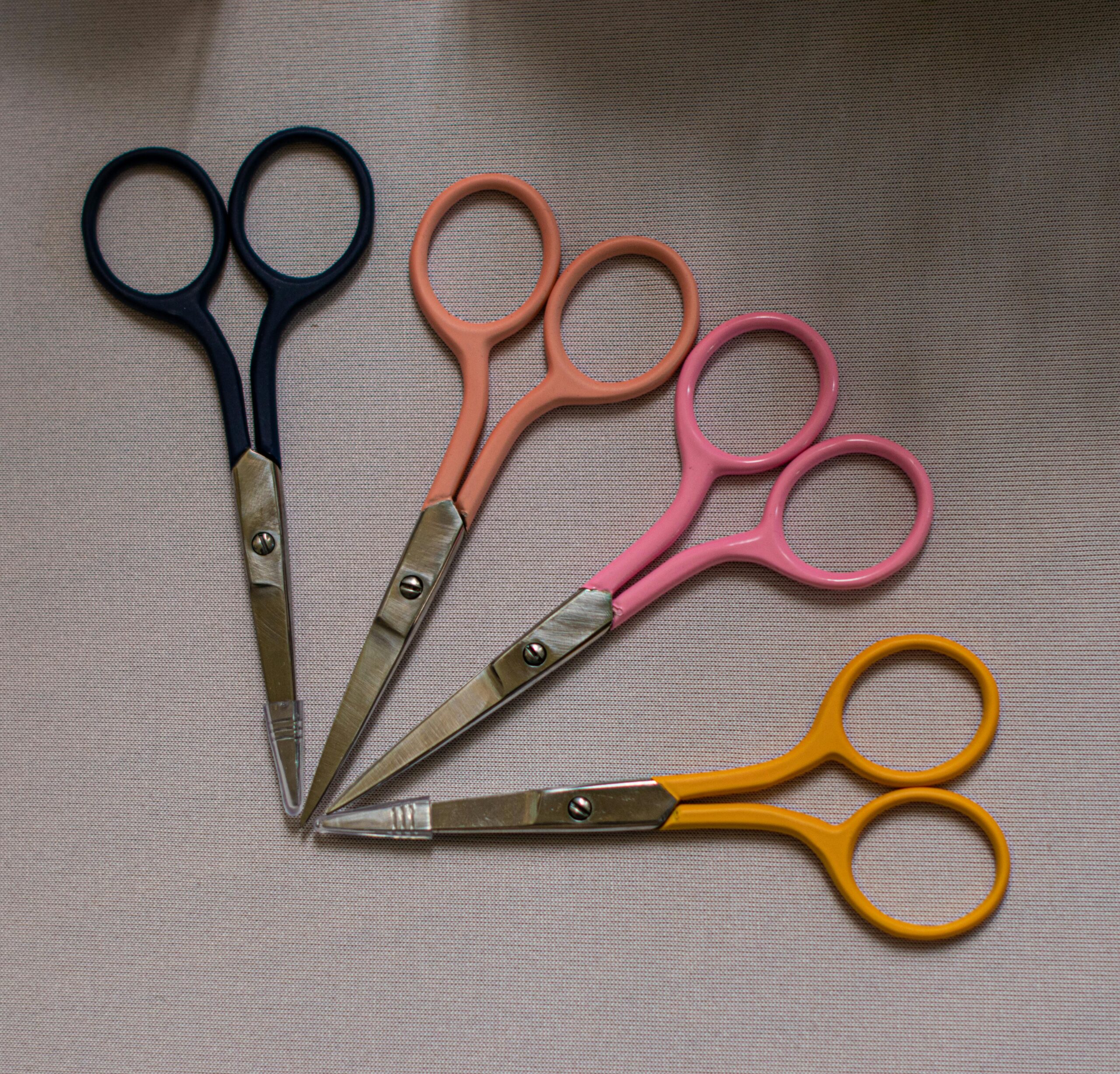Top view of five colorful scissors arranged in a fan shape on a gray surface.