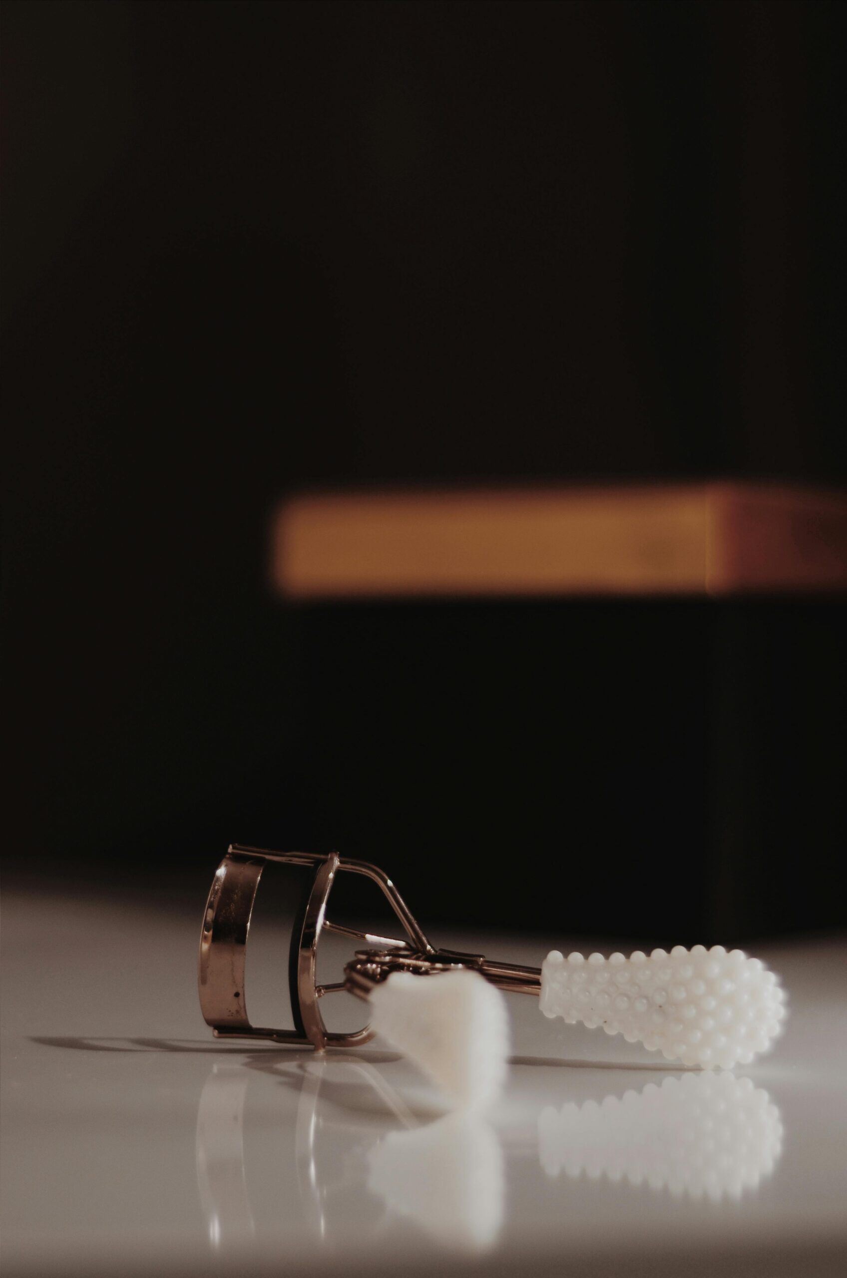 Close-up of an elegant eyelash curler resting on a light-reflective surface.