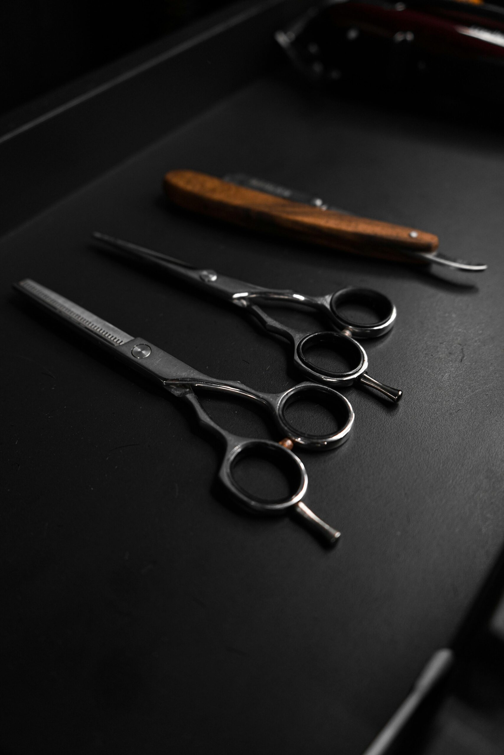 Close-up of various barbershop tools including scissors and razor on a dark background.