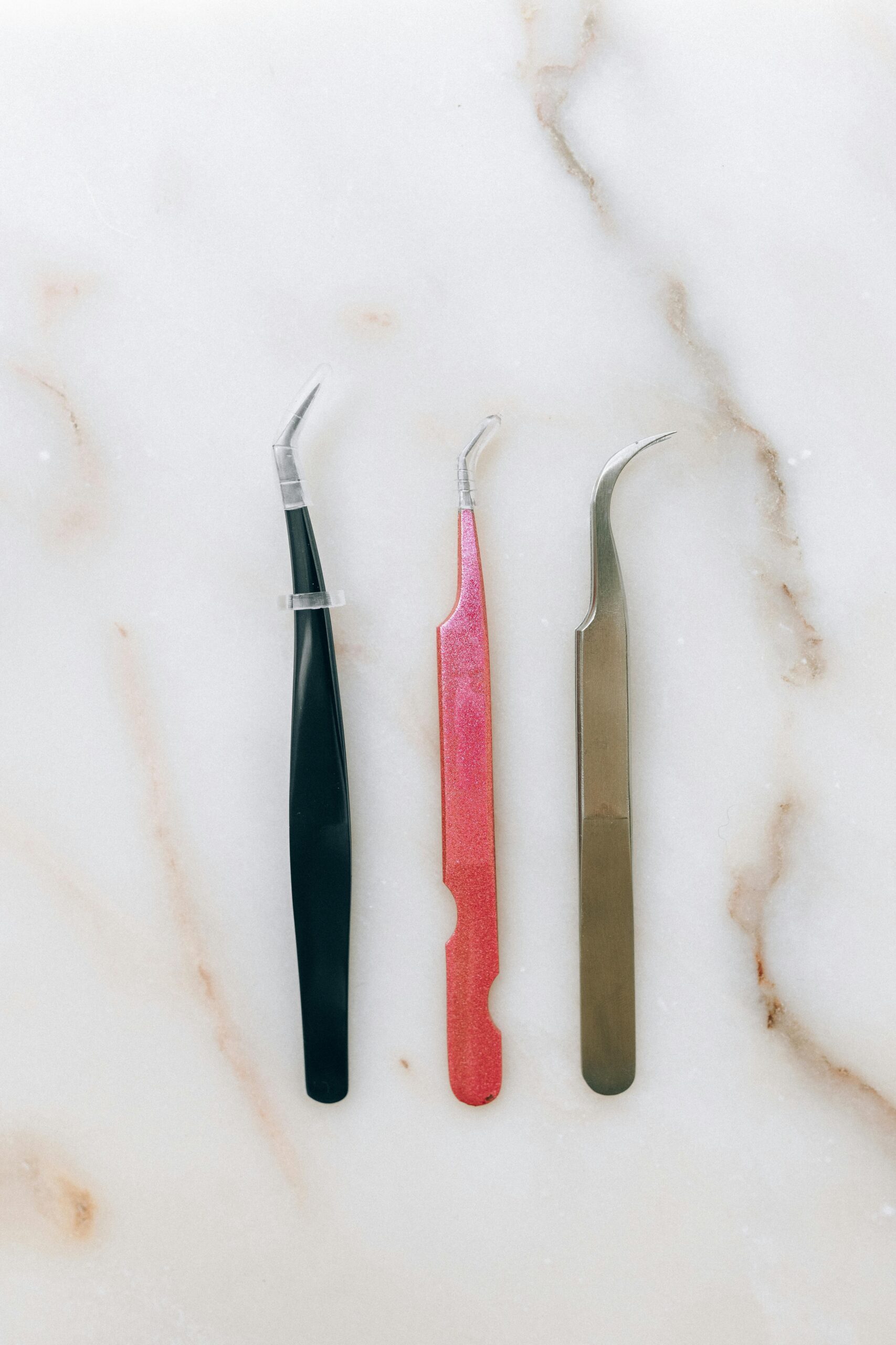 Three colorful tweezers on a marble surface, showcasing sharp stainless steel tips.