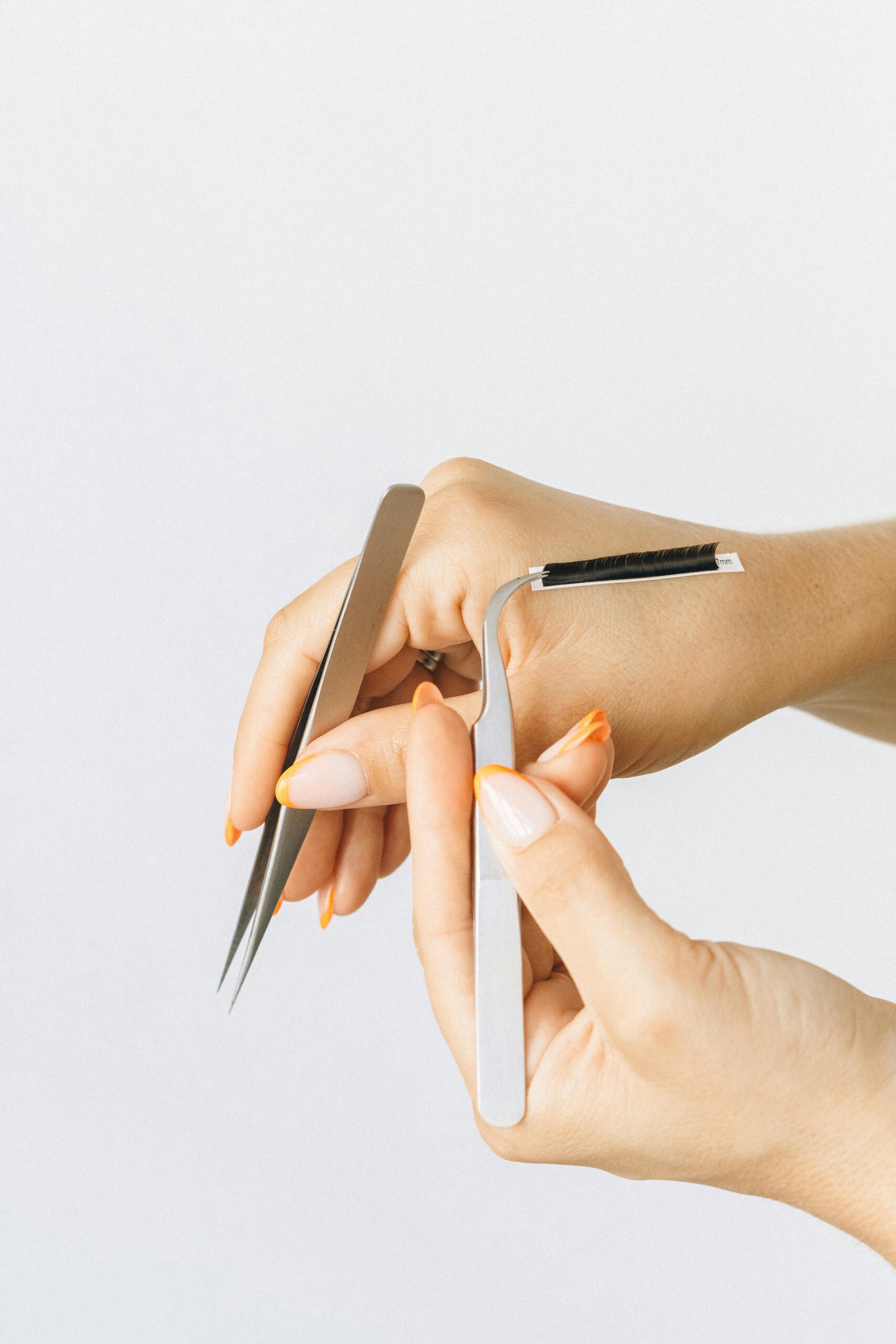 Close-up of hands using tweezers for eyelash extensions on white background.