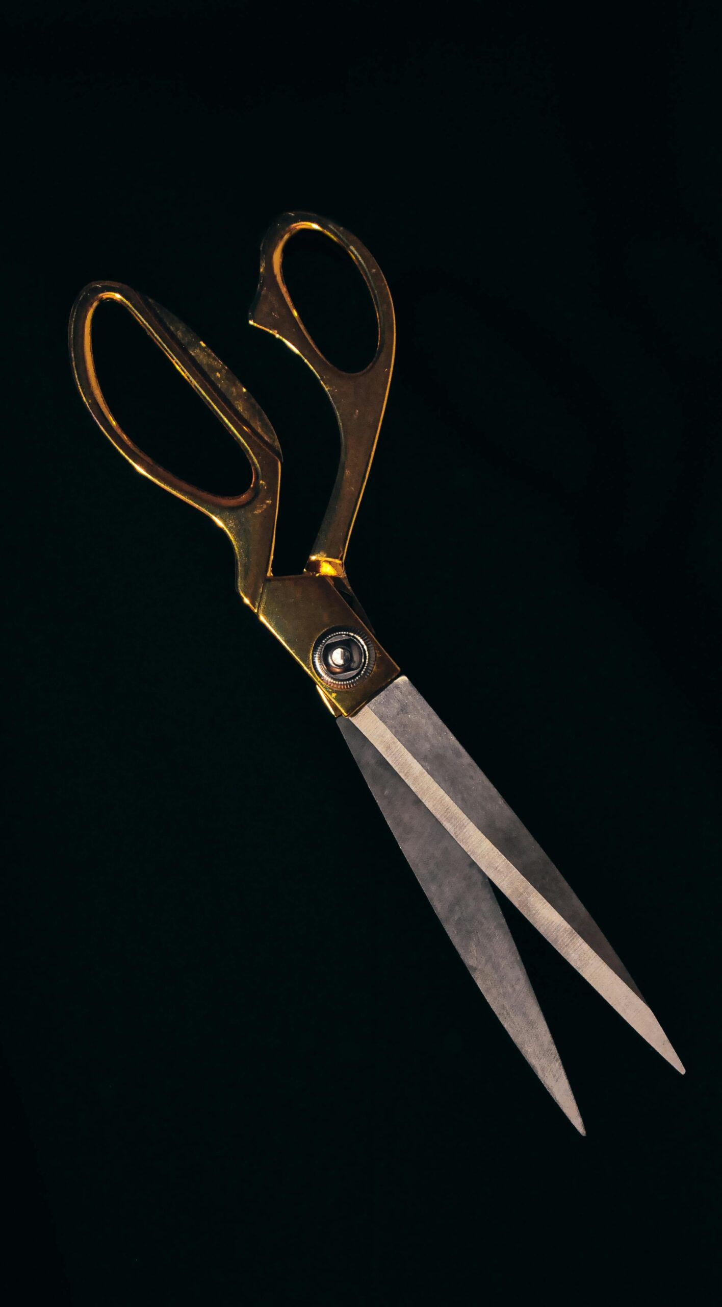 Stylish gold-handled scissors with sharp steel blades on a black backdrop, perfect for crafting themes.
