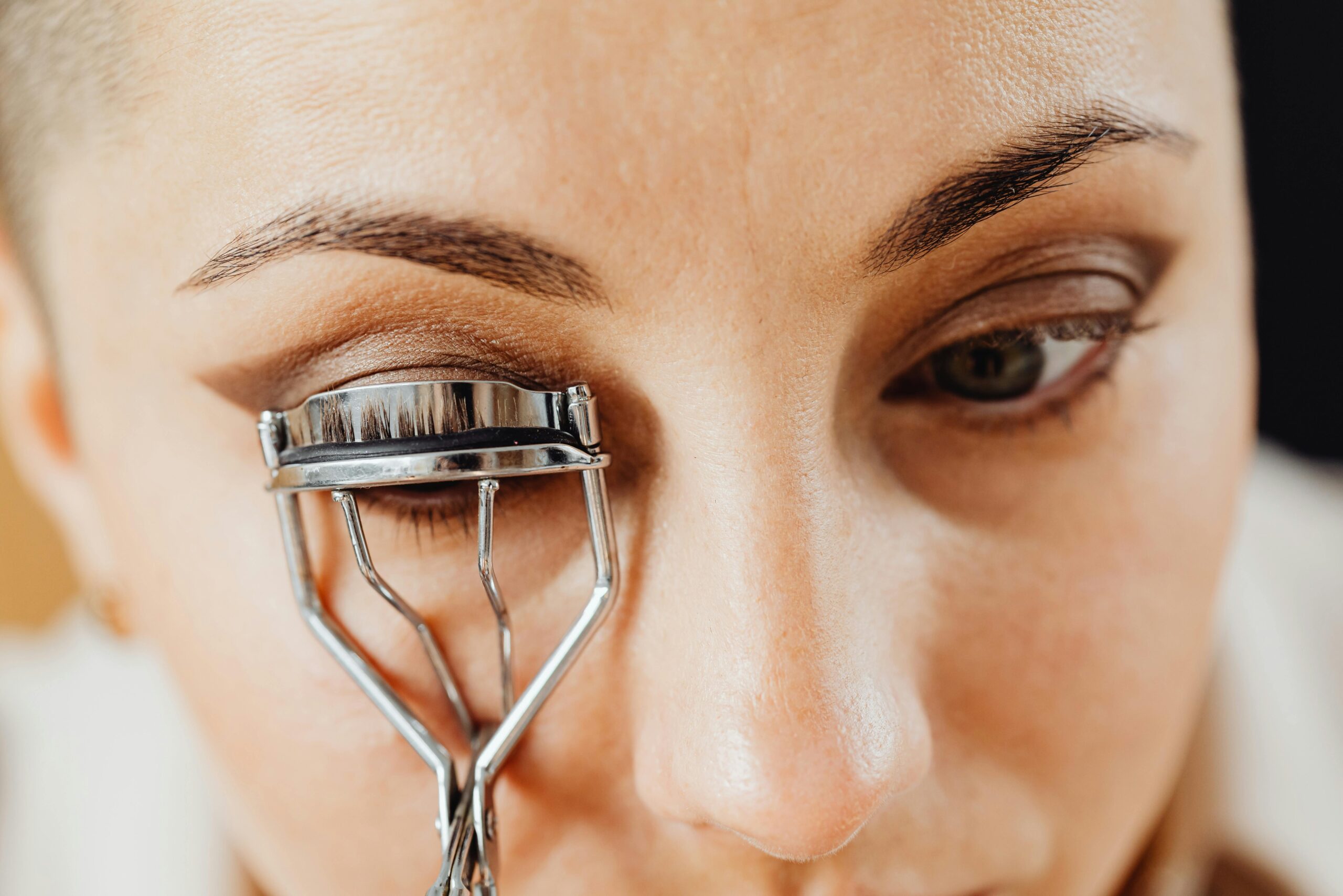 Detailed close-up of a woman applying an eyelash curler to her eye.